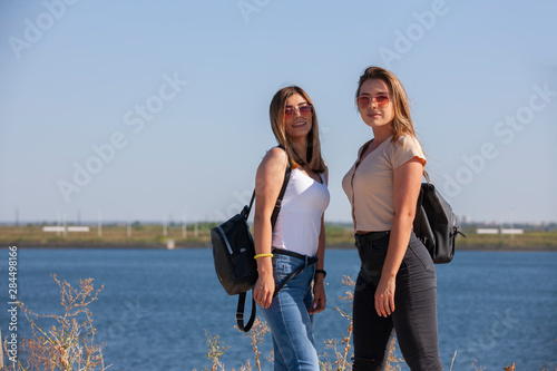 two beautiful young and stylish girl sitting in a summer city near water