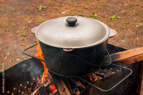 Open air kitchen at party picnic. Pilaf cooking on fire outdoor. Big pot closed with cover stays on wire rack and steams. Close up image of meal dish preparation