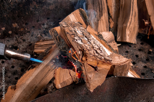 Fireplace kindling of chopped wood logs by gas torch. Method of firing at camping outdoor. Close up image of burning woods and flamethrower head