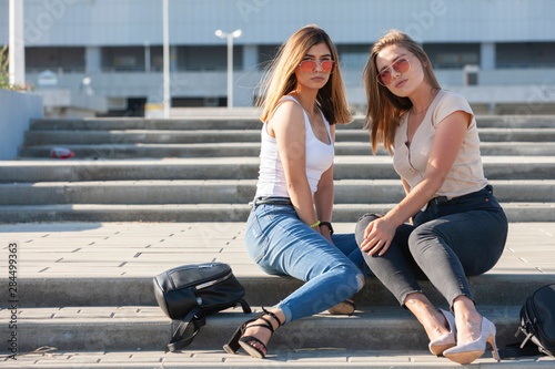 Two sexy girls sitting on a stairs. Outdoor fashion portrait