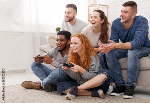 Diverse friends playing video games, sitting on floor at home