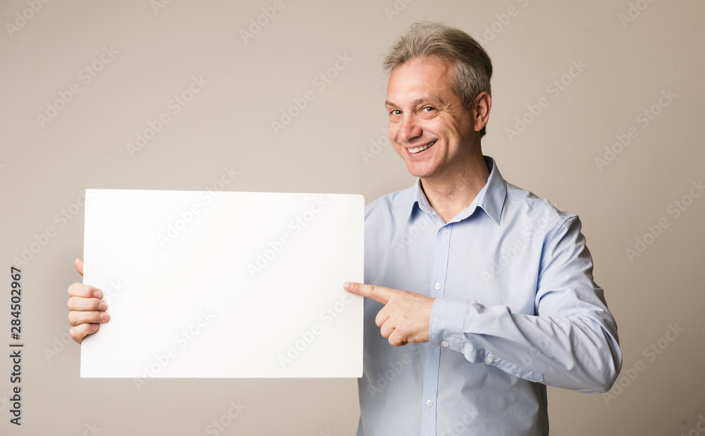 Mature man holding blank board and pointing on it Mature man holding blank board and pointing on it
