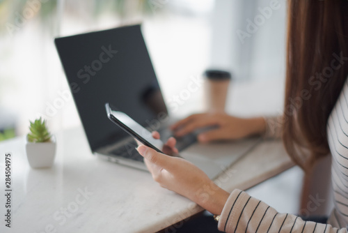 Closed up and focus on hand of young woman using a smartphone and have notebook put on table in background. Other hand put on a notebook. co working space concept.