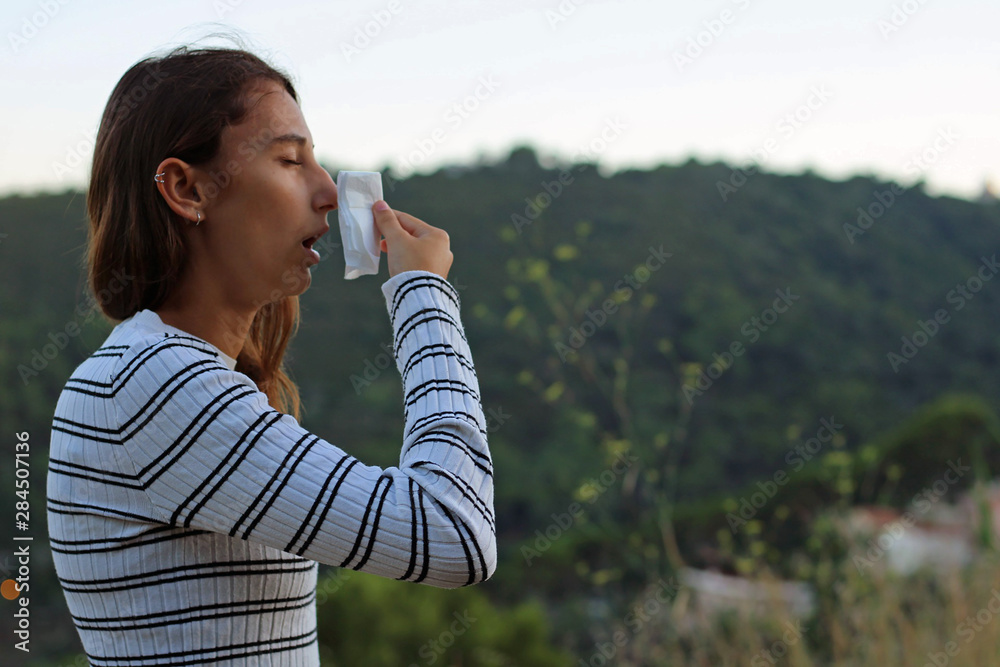 Health and medicine - Young woman sneezing in the woods with a handkerchief. Health and medicine - Young woman sneezing in the woods with a handkerchief.
