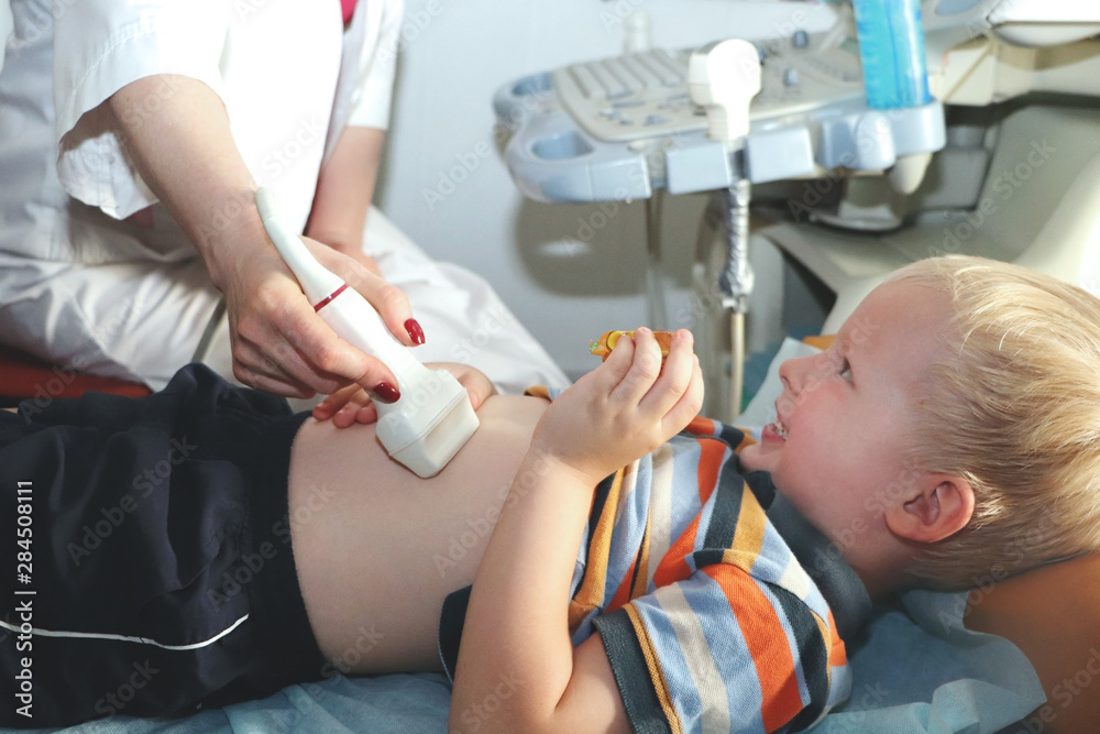 An ultrasound doctor makes an ultrasound of the abdominal cavity of the child. The boy is being examined in the office of the children's hospital An ultrasound doctor makes an ultrasound of the abdominal cavity of the child. The boy is being examined in the office of the children's hospital