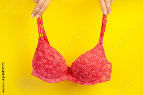 Fingers holding bra on yellw background.