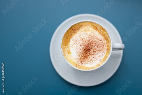 cup of cappuccino with cocoa powder on a blue background, view directly from above, copy space