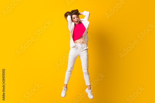 Young woman jumping over isolated yellow wall © luismolinero
