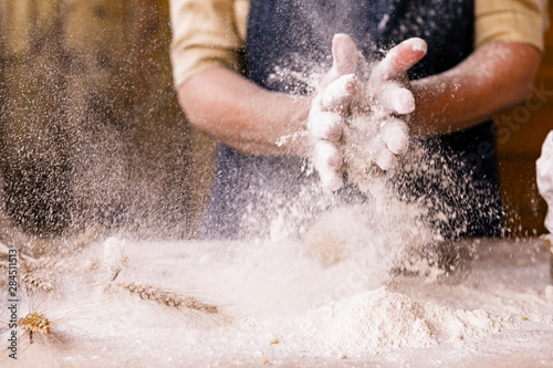 Women's hands, flour and dough.Levitation in a frame of dough and flour.A woman in an apron is preparing dough for home baking. Rustic style photo. Wooden table, wheat ears and flour. Emotional photo.