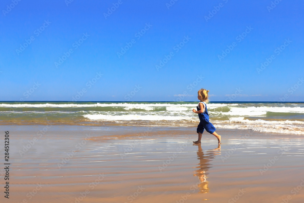 The girl is walking along the beach on a sunny day.