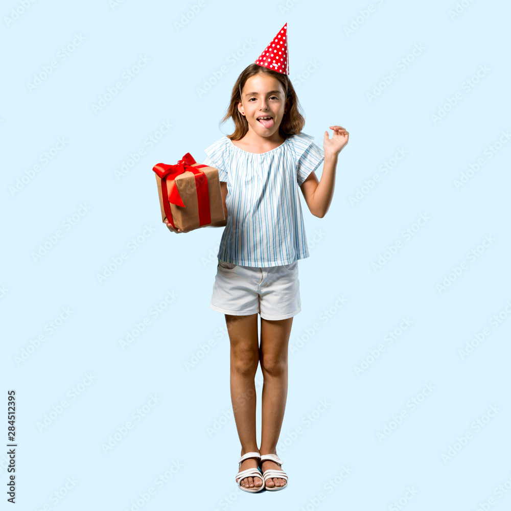 Full body of Little girl at a birthday party holding a gift showing tongue at the camera having funny look on blue background Full body of Little girl at a birthday party holding a gift showing tongue at the camera having funny look on blue background