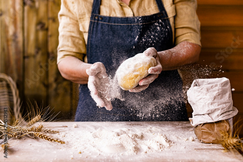 Women's hands, flour and dough. Levitation in a frame of dough and flour. A woman in an apron is preparing dough for home baking. Rustic style photo. Wooden table, wheat ears and flou.Emotional photo