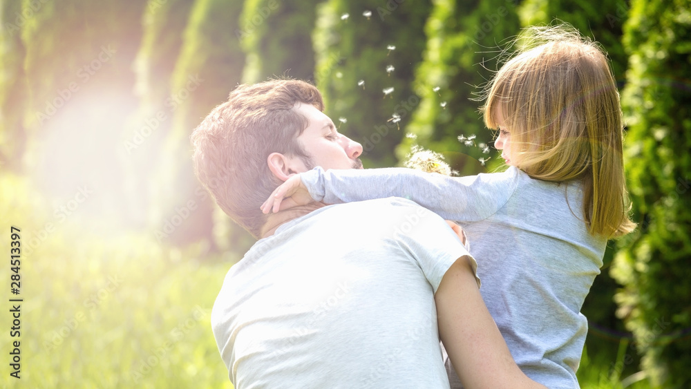 Father and daughter blowing dandelion flowers