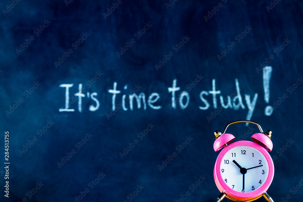 White chalk handwritten inscription of it is time to study in center of blackboard. Pink alarm clock on chalkboard background. Preparing pupils children students for university, college, academy. White chalk handwritten inscription of it is time to study in center of blackboard. Pink alarm clock on chalkboard background. Preparing pupils children students for university, college, academy.