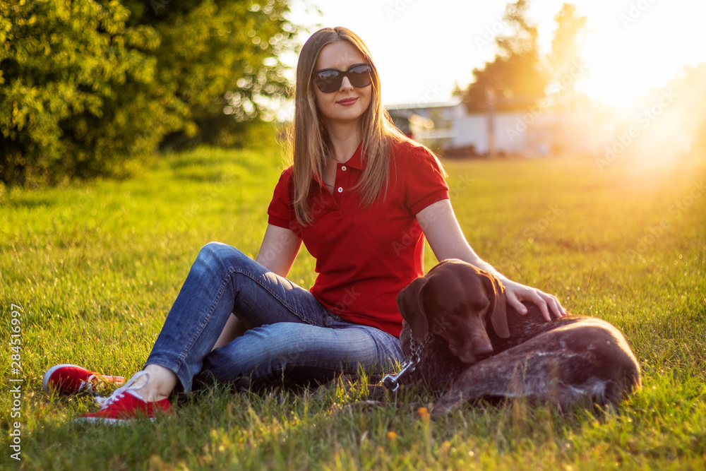 Girl in red clothing and sunglasses playing with the dog in the green