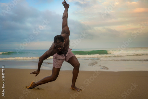 dramatic contemporary dance choreographer doing ballet beach workout, young attractive and athletic afro black American man dancing on sunrise