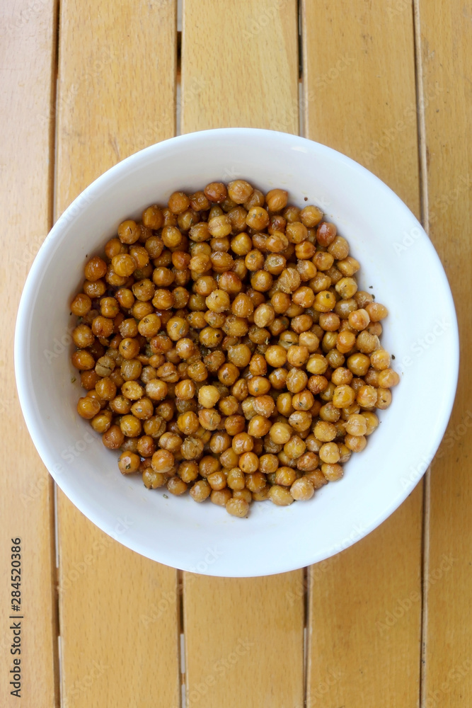 Bowl of roasted crispy chickpeas on wooden table. Top view. Bowl of roasted crispy chickpeas on wooden table. Top view.