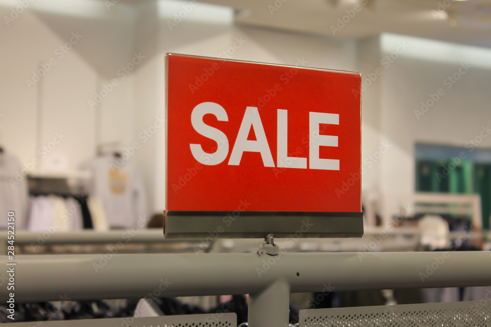 Red sale sign discount on clothing rack in modern shopping mall or department store with copy space. Business marketing advertising concept Red sale sign discount on clothing rack in modern shopping mall or department store with copy space. Business marketing advertising concept