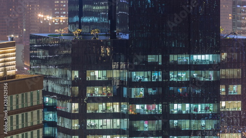 Lights in windows of modern multiple story office building in urban setting at night timelapse