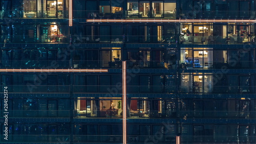 Lights in windows of modern multiple story building in urban setting at night timelapse