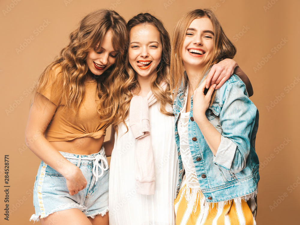 Three young beautiful smiling hipster girls in trendy summer casual clothes. Sexy carefree women posing on golden background. Positive models going crazy Three young beautiful smiling hipster girls in trendy summer casual clothes. Sexy carefree women posing on golden background. Positive models going crazy