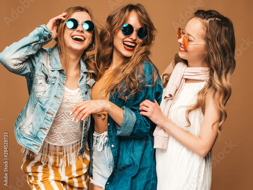 Three young beautiful smiling hipster girls in trendy summer casual clothes. Sexy carefree women posing on golden background. Positive models going crazy