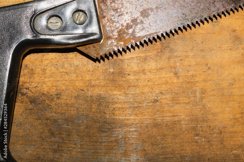 Old hand saw on a dirty wooden background. working area with hand instrument. carpentry tool. manual labor concept Old hand saw on a dirty wooden background. working area with hand instrument. carpentry tool. manual labor concept