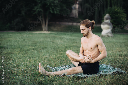 Yoga at park. Bearded man in lotus pose sitting on green grass. Concept of calm and meditation. photo