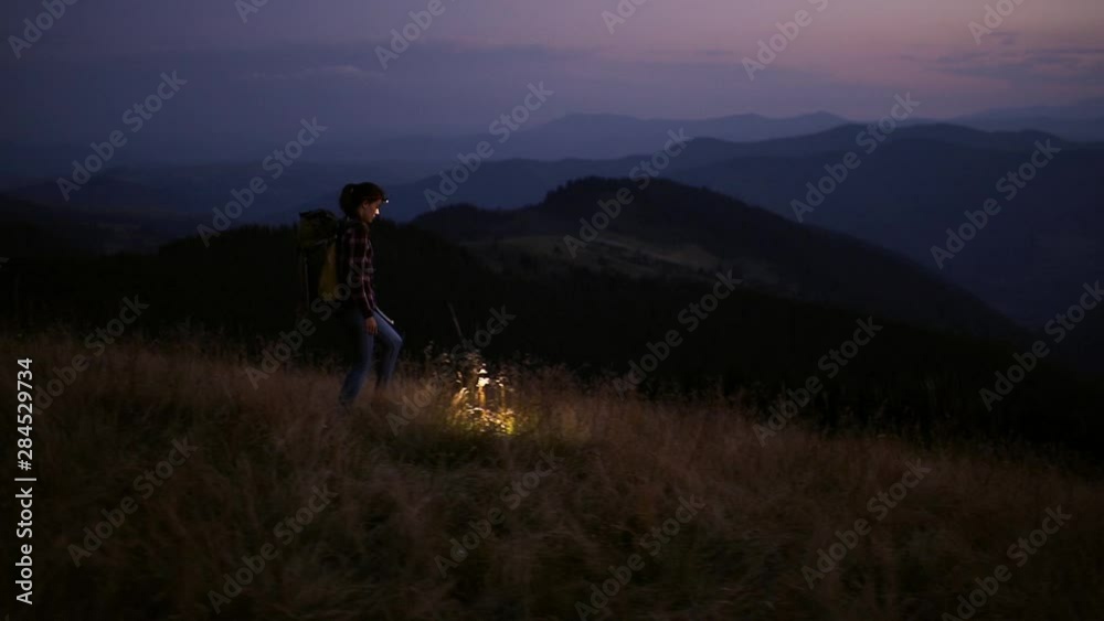 Happy woman traveler with headlamp flashlight hiking in the mountains. Summer adventure journey in mountain nature outdoors. A brilliant sunset over the mountains. High iso with Noise Happy woman traveler with headlamp flashlight hiking in the mountains. Summer adventure journey in mountain nature outdoors. A brilliant sunset over the mountains. High iso with Noise
