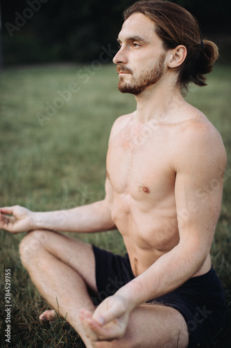 Yoga at park. Bearded man in lotus pose sitting on green grass. Concept of calm and meditation. photo