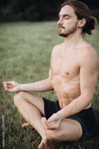 Yoga at park. Bearded man in lotus pose sitting on green grass. Concept of calm and meditation. photo