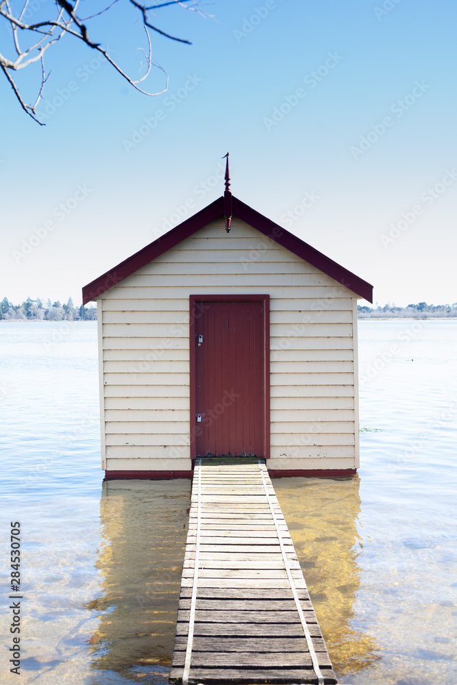 Small timber boatshed with red door on lake edge Small timber boatshed with red door on lake edge