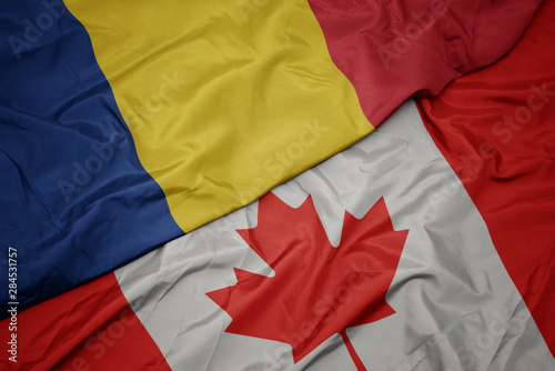 waving colorful flag of canada and national flag of romania.