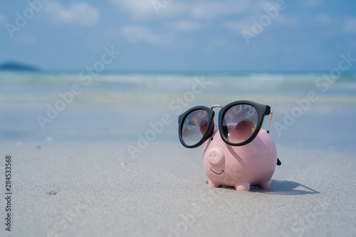 Pig piggy bank with sunglasses on the sand beach.