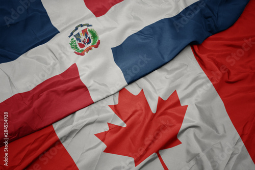 waving colorful flag of canada and national flag of dominican republic.