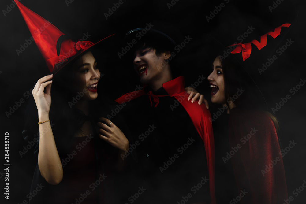 Obraz premium halloween portrait on dark background of man in vampire costume with two women in witch costume for halloween party with misty atmosphere