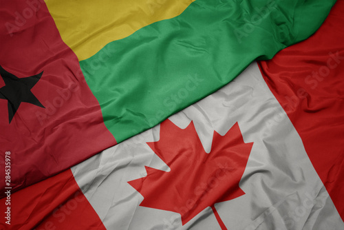 waving colorful flag of canada and national flag of guinea bissau.