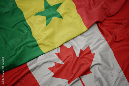 waving colorful flag of canada and national flag of senegal.