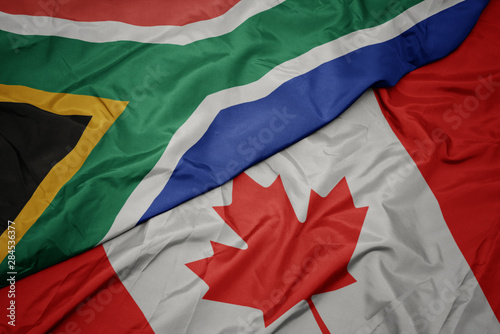 waving colorful flag of canada and national flag of south africa.