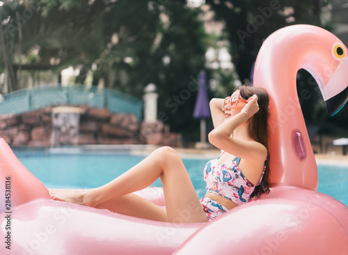 Asian young woman relax on pink flamingo inflatable looking up at pool villa © dodotone