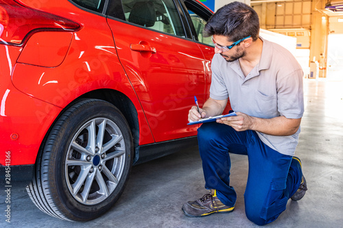 Technician with safety glasses checking the tires of a car during a vehicle inspection photo