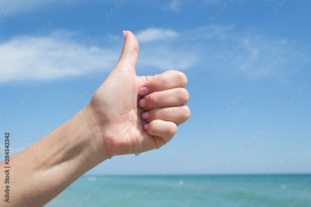 Sign with thumb up. Female hand against the sky and blue sea Sign with thumb up. Female hand against the sky and blue sea