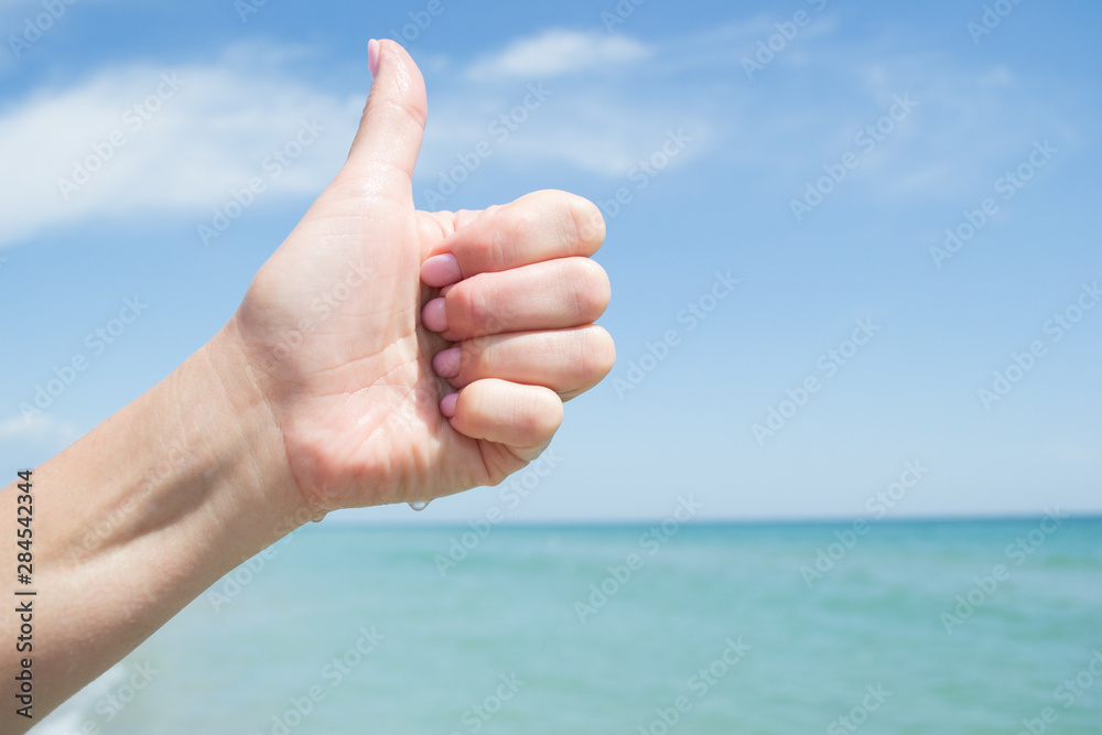 Sign with thumb up. Female hand against the sky and blue sea Sign with thumb up. Female hand against the sky and blue sea