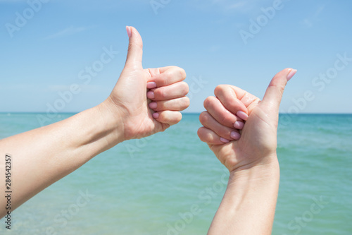 Sign with thumb up. Female hands against the sky and blue sea