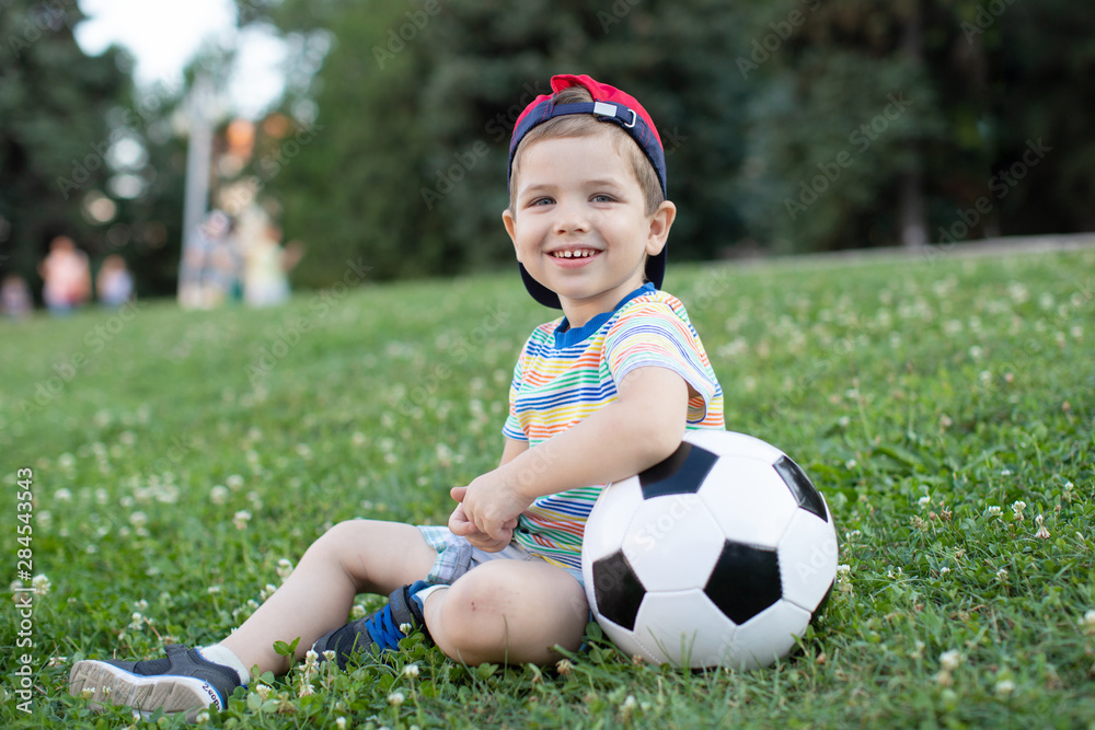 thoughtful little boy sits on the grass and put his hands on a soccer ball thoughtful little boy sits on the grass and put his hands on a soccer ball
