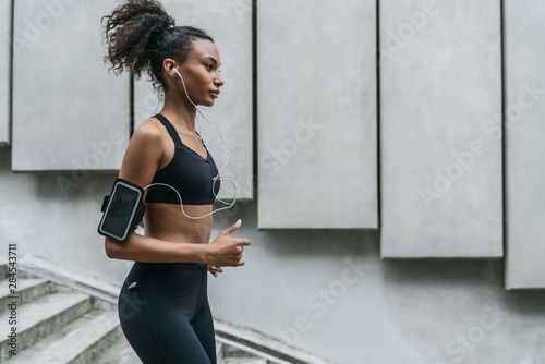 Young woman with earphones running on the steps as exercising outdoors in city