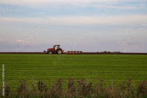 Roter Trecker plügt grünes Feld mit blauem Himmel