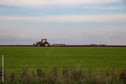 Roter Trecker plügt grünes Feld mit blauem Himmel