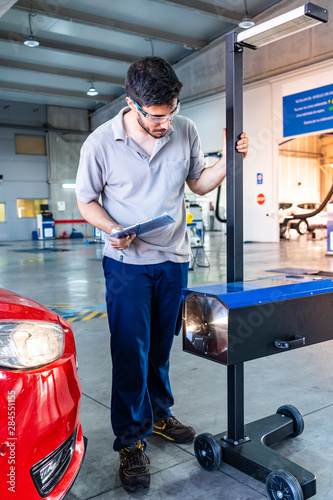Technician with safety glasses checking the head lights of a car during a vehicle inspection