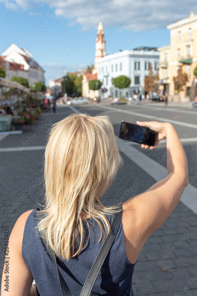 A girl is making selfie with smartphone on the square in Old Town.